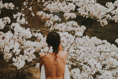 赤裸上身的人站在白色花瓣的花边